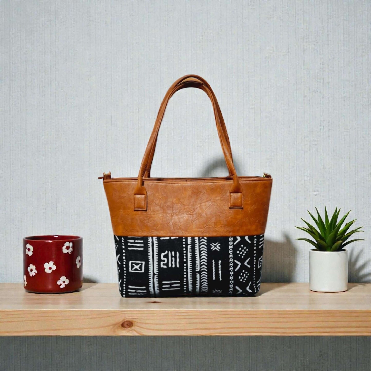Imani Heritage Luxe Tote – Custom Handcrafted Mudcloth & Leather Bag on a wooden shelf with plants.