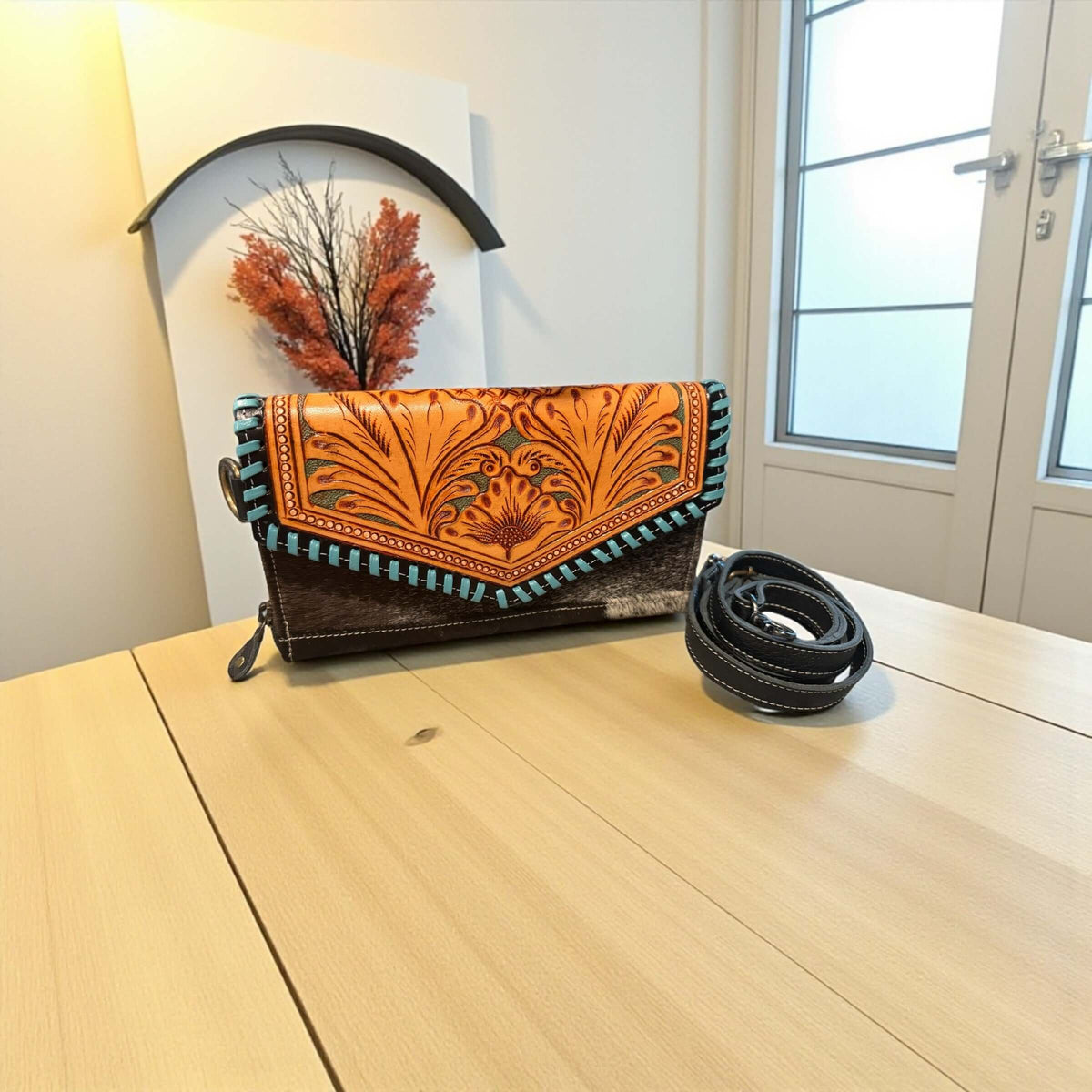 Bloom Cowhide Crossbody Wallet on a table, showcasing hand-tooled floral flap and turquoise detailing.