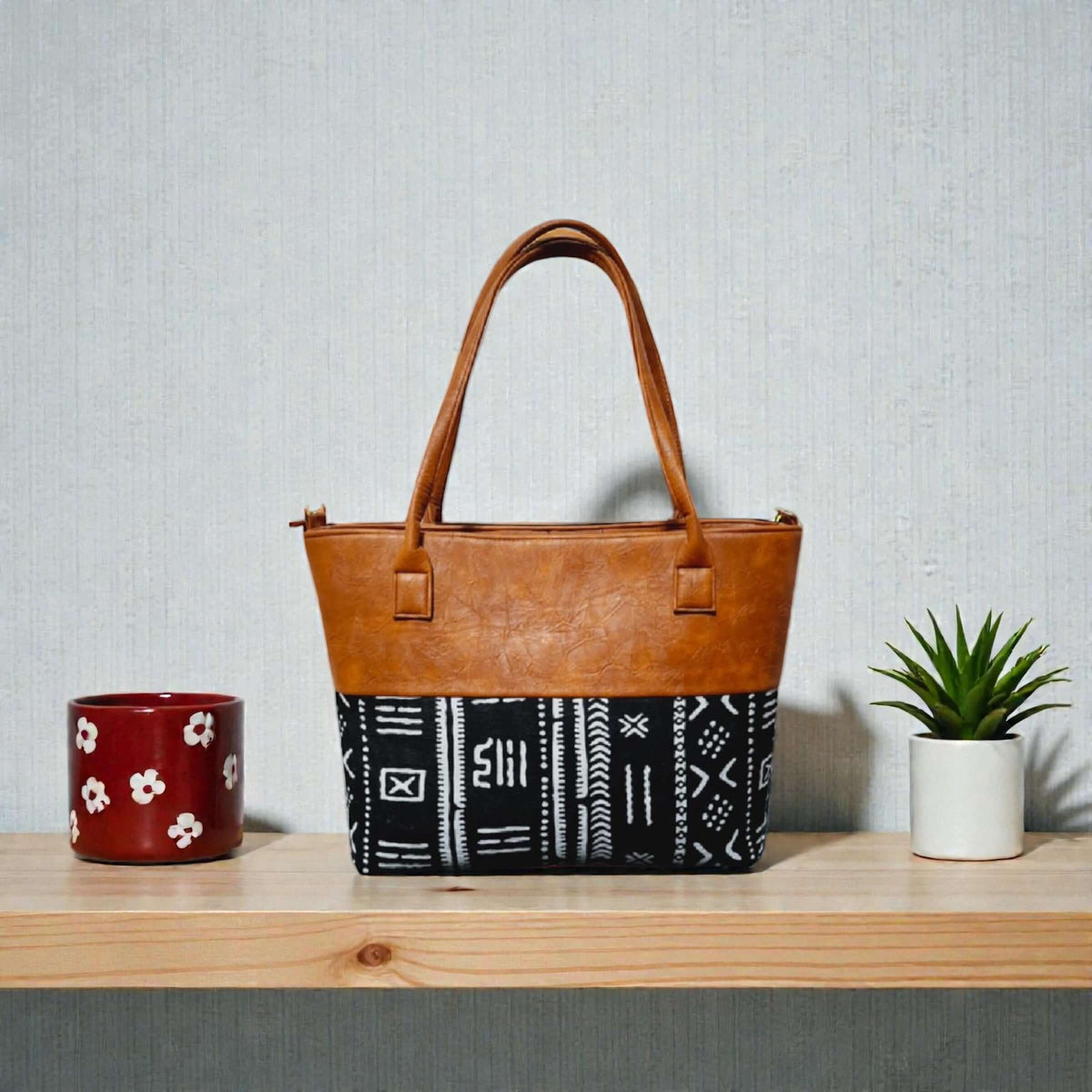 Imani Heritage Luxe Tote – Custom Handcrafted Mudcloth & Leather Bag on a wooden shelf with plants.