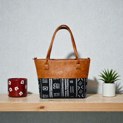 Imani Heritage Luxe Tote – Custom Handcrafted Mudcloth & Leather Bag on a wooden shelf with plants.