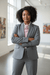 Confident woman in grey suit with blush ascot, showcasing chic style in a gallery, embodying elegance and professionalism.