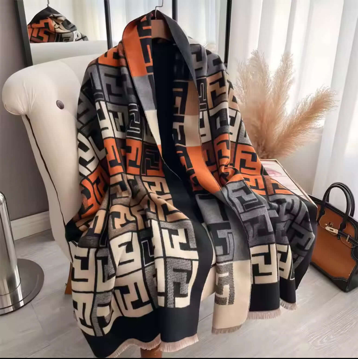 Geometric Luxe Shawl displayed on a chair, showcasing its bold geometric print in warm orange and neutral tones.