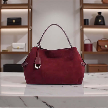 Cranberry Luxe Suede Bag displayed on a marble table, showcasing its rich cranberry suede and boutique-inspired design.
