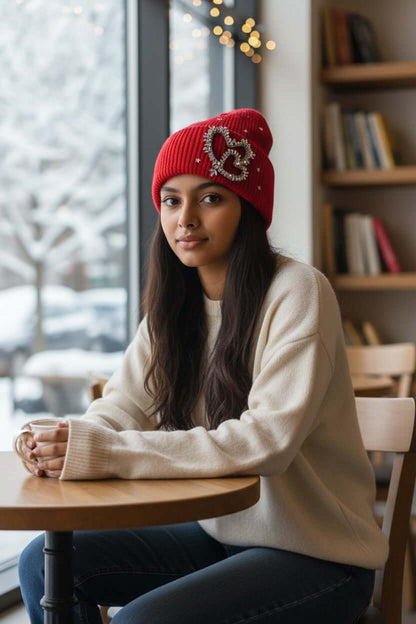 Legacy Luxe 'Crimson Heart Spark Beanie' worn by a model in a cozy café setting, showcasing its festive design.