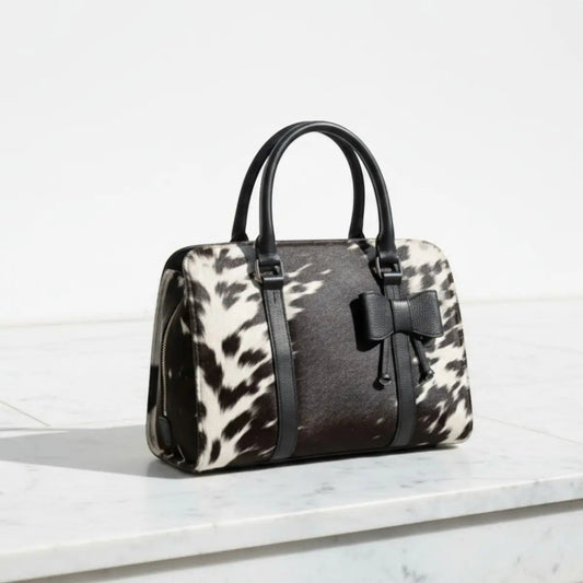 Legacy Dealz Wyatt cowhide crossbody bag with black leather trim and bow accent. Features black and white cowhide pattern.