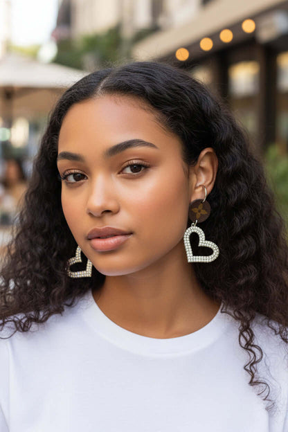 Model showcasing Crystal Heart Drop Earrings with diamond-studded crystal accents on a city street.